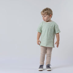 A young child wearing a stylish green striped t-shirt, standing upright with a relaxed posture. The t-shirt has short sleeves, a round neckline, and soft organic cotton fabric. The background is neutral, keeping the focus on the child and the t-shirt’s design.