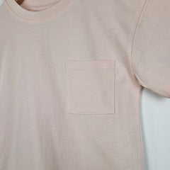 Flat lay close up image of a blush pink kids t-shirt, showing the front design which features a pocket on the left side.