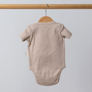 Back view of oat short sleeve baby bodysuit displayed on a wooden hanger, highlighting soft ribbed fabric and minimal seam design.