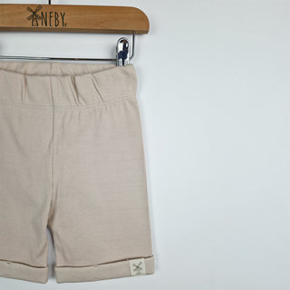 Front close up view of oat ribbed organic cotton kids shorts hanging on a wooden hanger, with neutral background.