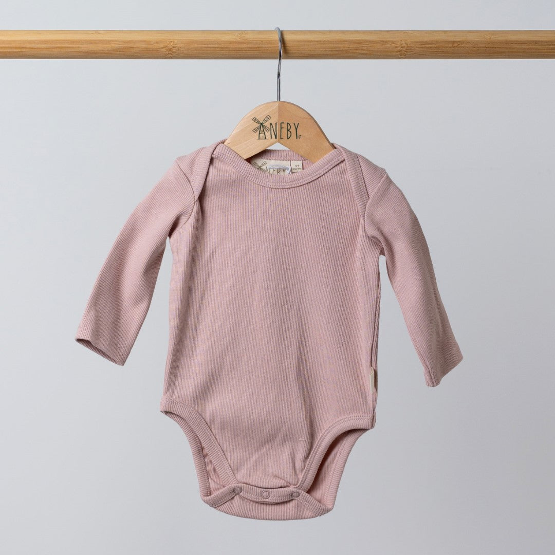 Dusty pink ribbed bodysuit with long sleeves for babies, hanging on a rail alongside other neutral-coloured pieces.