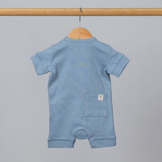 Slate blue short sleeve rib baby romper hanging, back view, with pocket and Aneby hem tag visible.