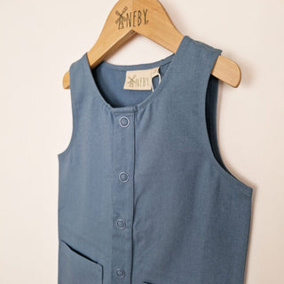 kids sleeveless overall in slate blue, front close up view showing front popper placket and binding neck stitching detail, displayed against a neutral background.
