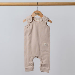 Oat-coloured sleeveless rib baby romper hanging on a wooden frame, front view. Neutral background.